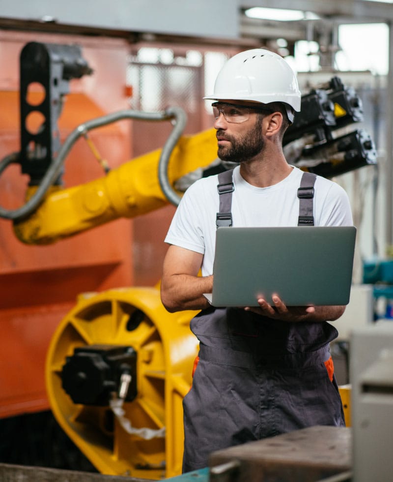 Arbeiter in einer Fabrik, der einen Laptop in der Nähe von Robotermaschinen benutzt