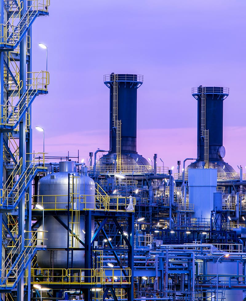 Große Industrieanlage mit Türmen, Tanks und Rohren in der Abenddämmerung.