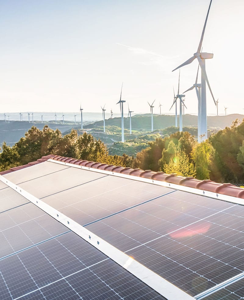 Solarmodule auf einem Dach und Windkraftanlagen an einem Hang als Beispiel für die Integration dezentraler Energiequellen (DER).